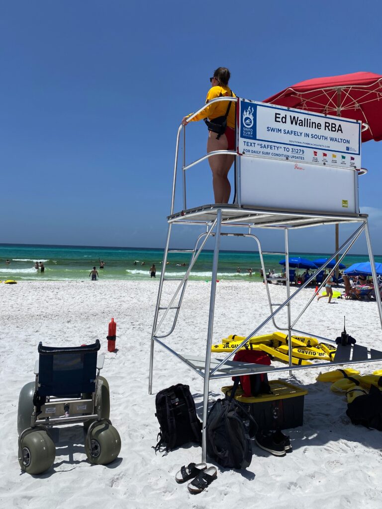 Image of a life guard in a life guard stand. There is also a beach wheelchair