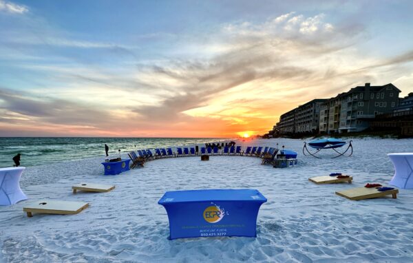 Private beach bonfire setup for 29 guests with tiki torches, side tables, and sunset views in Miramar Beach